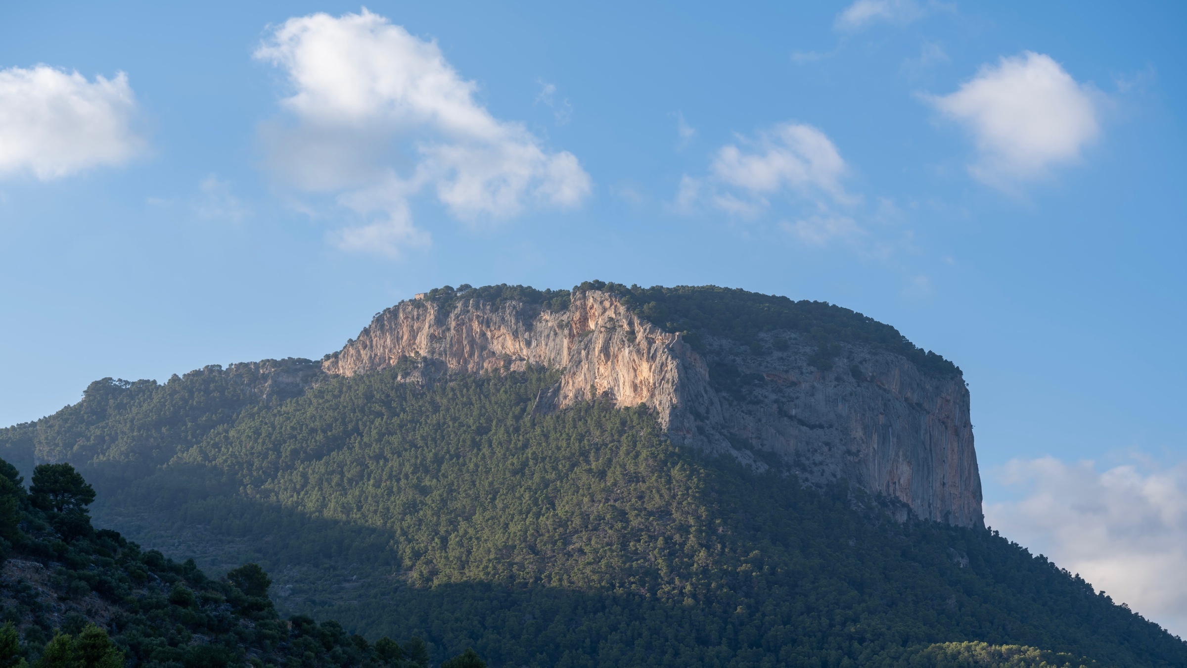Montaña iluminada entre pinos y nubes, en Mallorca