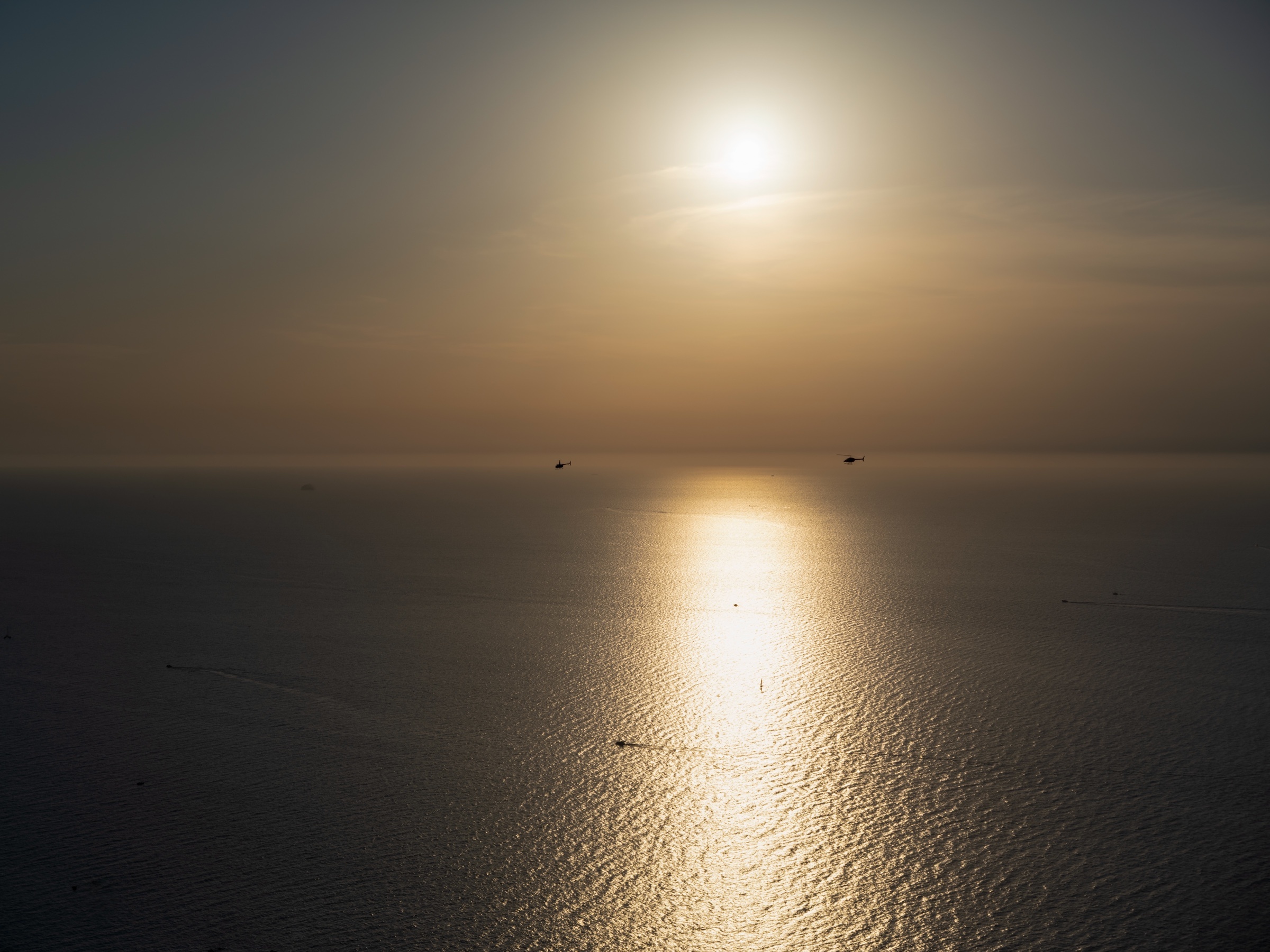 Sol sobre el mar y dos helicópteros en el horizonte